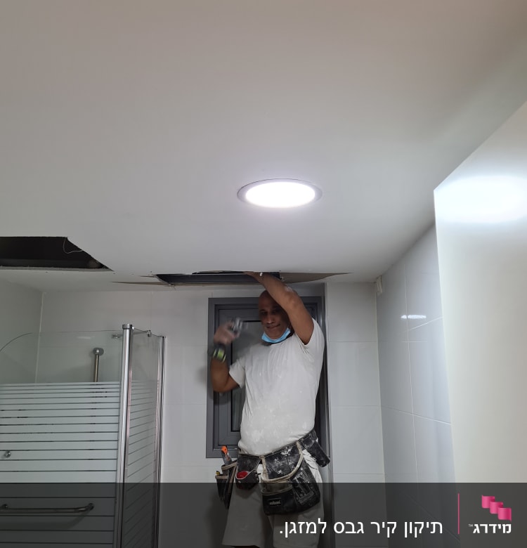 אדם מתקין לוח גבס בתקרה בחדר אמבטיה